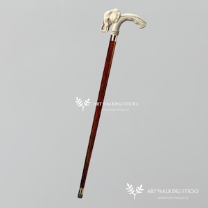 May include: A wooden walking stick with a silver elephant head handle. The stick is brown and has a dark brown finish. The elephant head is detailed and has a trunk that is curled up. The stick is about 36 inches long.