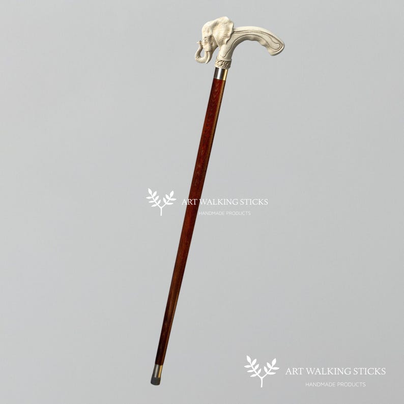 May include: A wooden walking stick with a silver elephant head handle. The stick is brown and has a dark brown finish. The elephant head is detailed and has a trunk that is curled up. The stick is about 36 inches long.