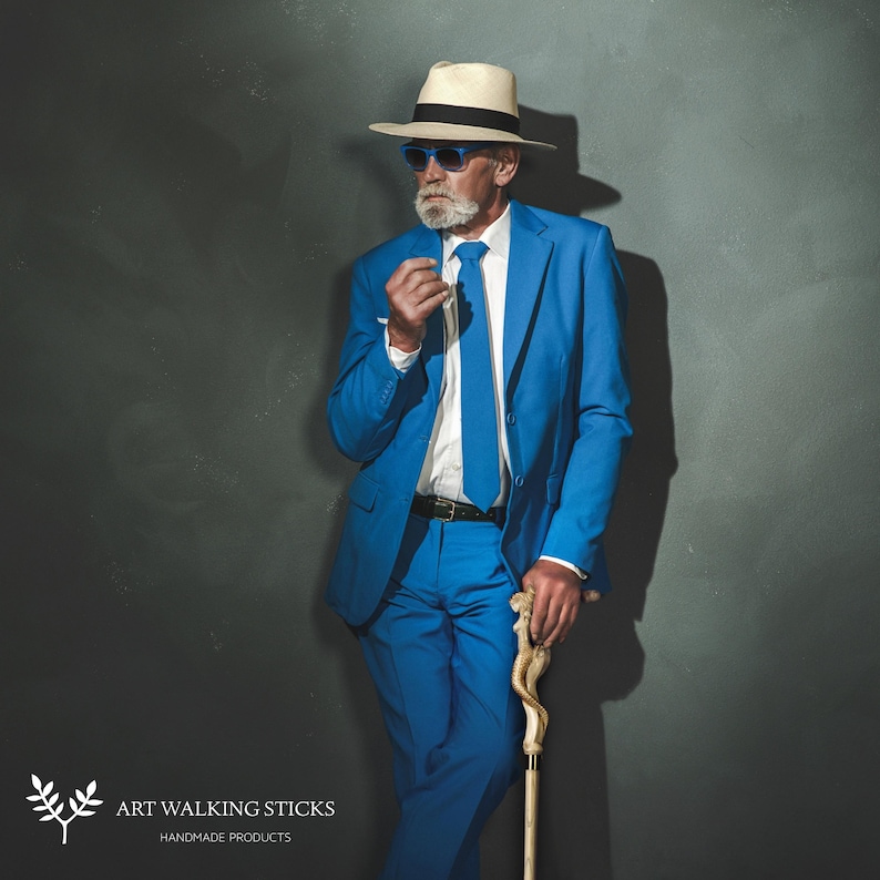 Puede incluir: Un hombre con un traje azul y un sombrero de paja con gafas de sol azules sostiene un bast&oacute;n de madera. El bast&oacute;n tiene un dise&ntilde;o tallado.