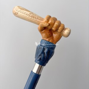 May include: A wooden walking stick with a carved hand holding a baseball bat. The bat is inscribed with the word "Yankees". The stick is painted blue and has a silver metal shaft.