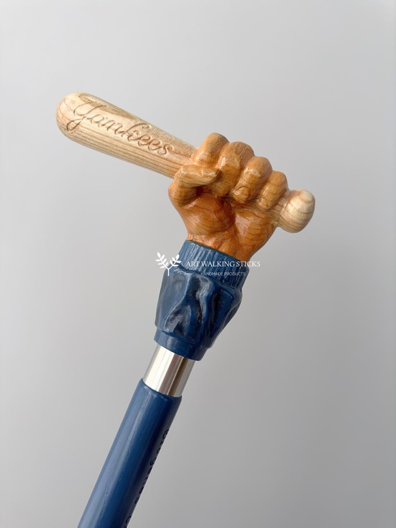 May include: A wooden walking stick with a carved hand holding a baseball bat. The bat is inscribed with the word "Yankees". The stick is painted blue and has a silver metal shaft.