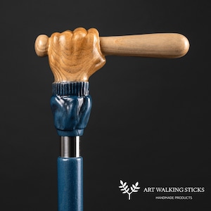 May include: A wooden walking stick with a carved hand holding a baseball bat. The hand is painted blue and the bat is natural wood. The stick is made of dark blue wood.