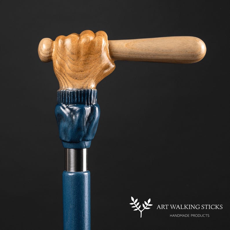 May include: A wooden walking stick with a carved hand holding a baseball bat. The hand is painted blue and the bat is natural wood. The stick is made of dark blue wood.