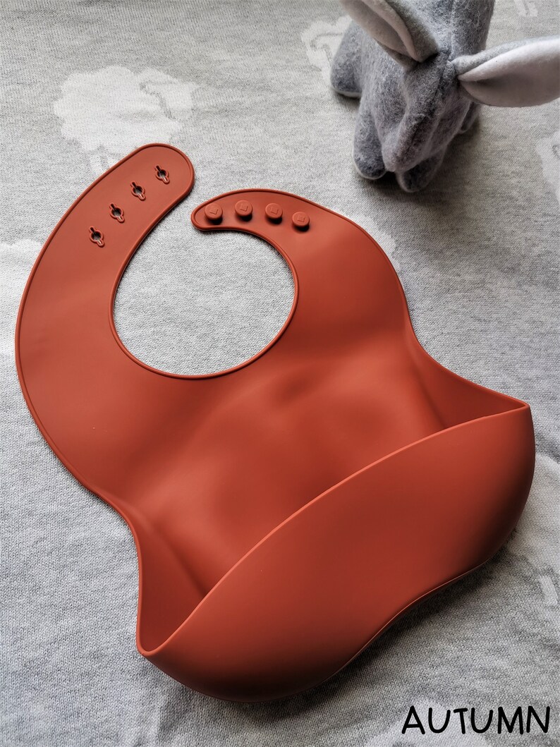 Puede incluir: Un babero de silicona color &oacute;xido para beb&eacute; con cuello ajustable y bolsillo curvo. El babero tiene una superficie lisa y est&aacute; dise&ntilde;ado para una f&aacute;cil limpieza. La palabra "AUTUMN" est&aacute; impresa en la parte inferior.