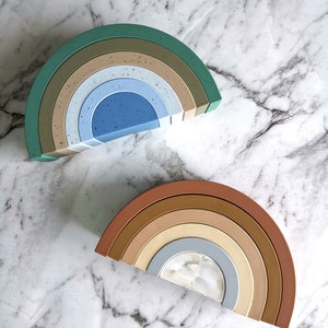 Könnte beinhalten: Zwei Regenbogen-Stapelbögen, einer in Grün- und Blautönen, der andere in Braun- und Beigetönen. Die Bögen sind aus Silikon und für Kinderspielzeug konzipiert.