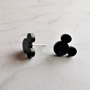 Könnte beinhalten: Ein Paar schwarze Mickey Mouse-förmige Ohrstecker. Die Ohrringe sind aus einem glatten, matten Material gefertigt.