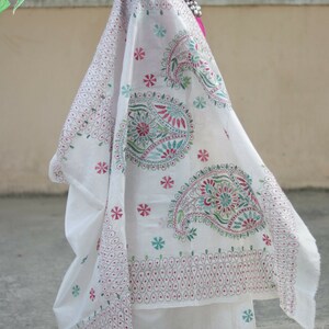 Puede incluir: Tela blanca bordada con dise&ntilde;os de cachemir y florales en rojo, verde y turquesa. La tela est&aacute; drapeada sobre un maniqu&iacute;, mostrando las intrincadas puntadas y el patr&oacute;n. El texto "Sui Dhaga @ Etsy.com" es visible.