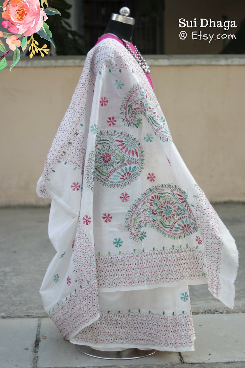 Puede incluir: Tela blanca bordada con dise&ntilde;os de cachemir y florales en rojo, verde y turquesa. La tela est&aacute; drapeada sobre un maniqu&iacute;, mostrando las intrincadas puntadas y el patr&oacute;n. El texto "Sui Dhaga @ Etsy.com" es visible.
