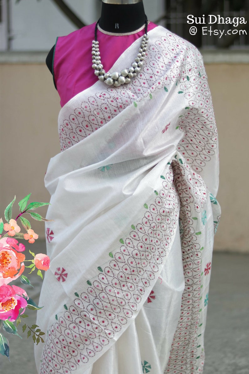Puede incluir: Sari blanco con intrincados detalles bordados en rojo, verde y azul. El sari est&aacute; drapeado sobre un maniqu&iacute;, combinado con una blusa fucsia y un collar de cuentas plateadas. El texto "Sui Dhaga @ Etsy.com" es visible.