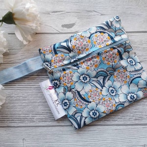 Puede incluir: Una bolsa azul con cremallera con un estampado floral. La bolsa tiene una correa azul claro y una etiqueta blanca con el texto "KK Fabrics & Creations".