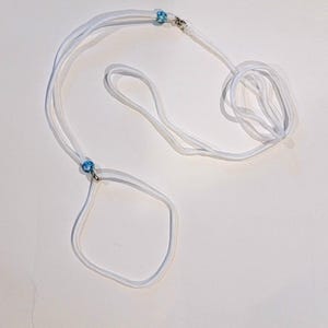 Può includere: Guinzaglio per cani bianco con perline blu e bianche. Il guinzaglio è realizzato in un materiale sottile e flessibile e ha una fibbia in metallo.