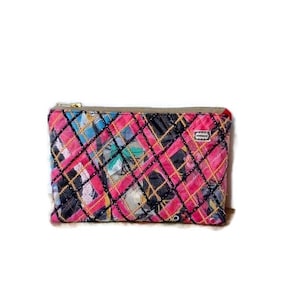 Könnte beinhalten: Eine rosafarbene und schwarze gesteppte Kosmetiktasche mit Reißverschluss. Die Tasche hat ein geometrisches Muster und ist aus einem weichen, strukturierten Stoff gefertigt.