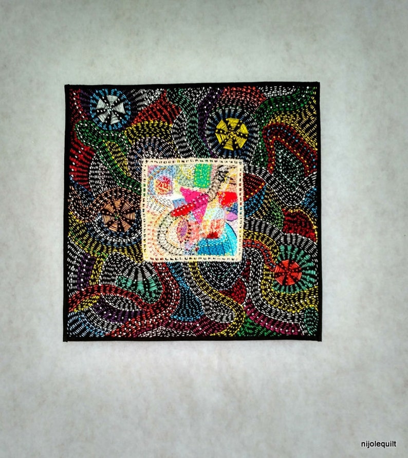 May include: A colorful, abstract quilt with a black background. The quilt is made of various fabrics and materials, including beads and sequins. The quilt features a central square with a colorful, abstract design.