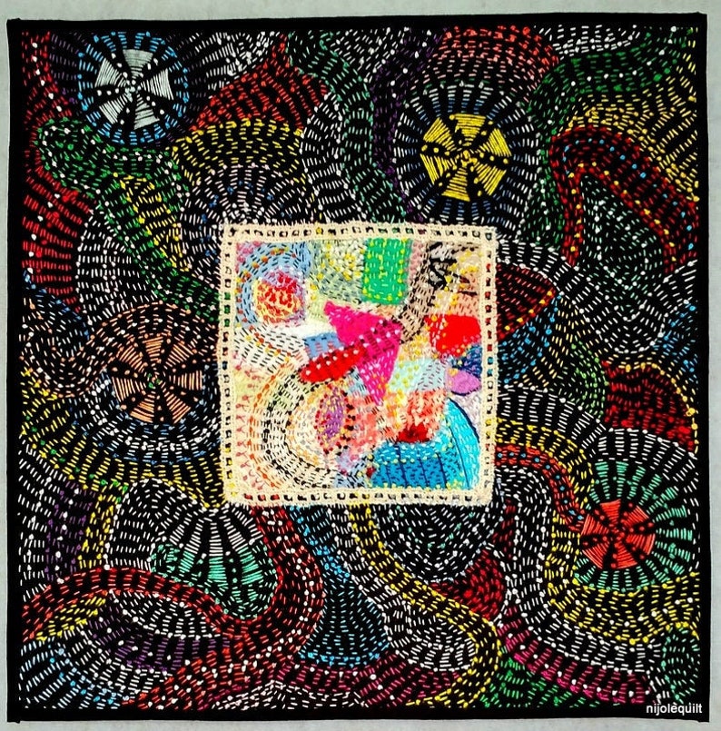 May include: A black fabric square with a colorful embroidered design. The design features a central square with abstract shapes and swirls in various colors, surrounded by a border of smaller, repeating swirls in black, white, and yellow.