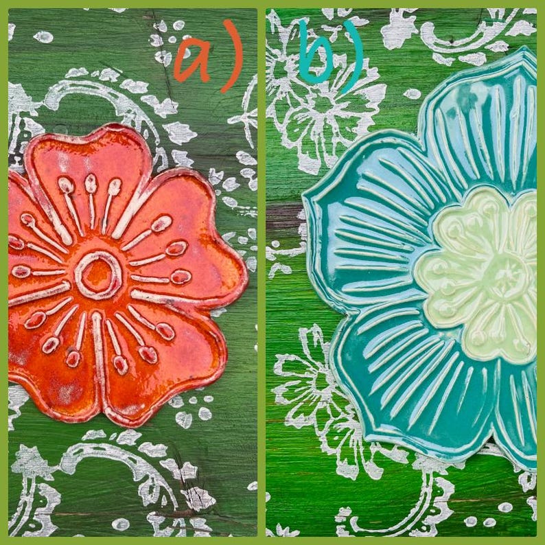 May include: Two ceramic flower-shaped decorations. One is orange with a textured surface, the other is teal with a light green center. Both are on a green background with a white floral pattern. The flowers have a glossy finish.