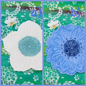 May include: Two ceramic flower-shaped decorative plates. One is white with a light blue center, the other is blue with a darker blue center. The plates are on a green and white patterned surface, with white orchids.
