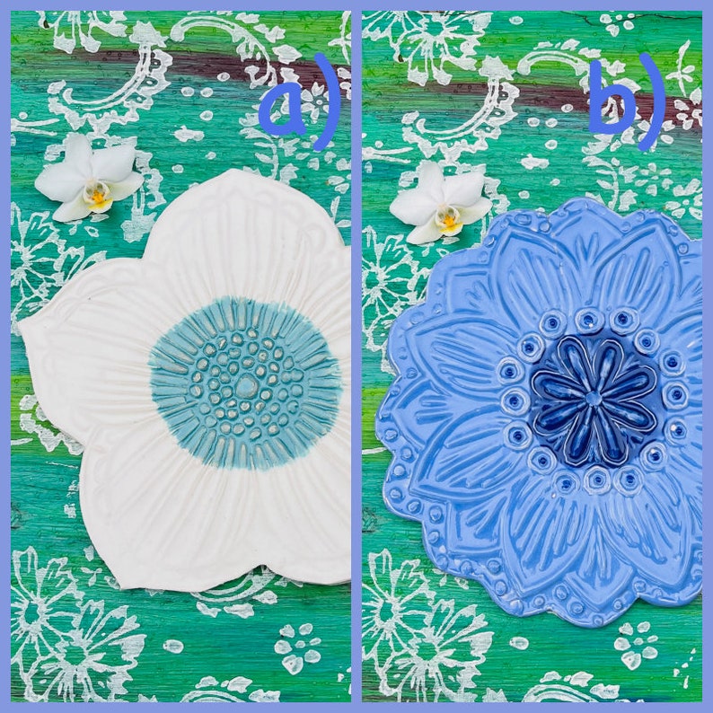 May include: Two ceramic flower-shaped decorative plates. One is white with a light blue center, the other is blue with a darker blue center. The plates are on a green and white patterned surface, with white orchids.