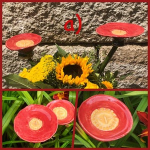 Könnte beinhalten: Drei rote Keramik-Vogelhäuschen mit gelbem Mittelteil. Die Futterhäuschen sind auf Metallstielen und in einer Reihe angeordnet.