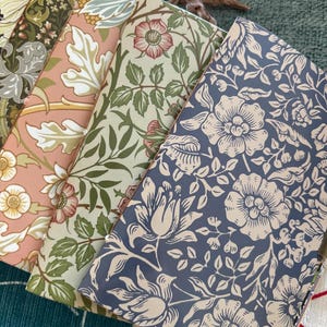 Könnte beinhalten: Eine Sammlung von Notizbüchern mit floralen Mustern in verschiedenen Farben. Die Notizbücher weisen Designs in Rosa, Grün und Blau mit detaillierten botanischen Illustrationen auf. Die Einbände haben eine Vintage-Ästhetik mit goldfarbenen Eckenschützern.