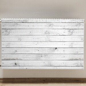 Op de afbeelding: Witte radiator met een houtnerfpatroon. De radiator is gemonteerd op een witte muur.