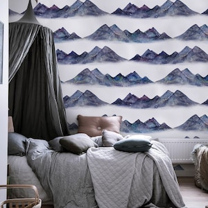May include: A bedroom with a canopy bed and a mountain range wallpaper. The wallpaper features a watercolor design of blue and purple mountains with white stars. The bed is made with a gray duvet and pillows.