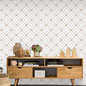 May include: A wooden media console with three drawers and open shelves. The console is in front of a white wall with a geometric pattern in brown lines. The console is decorated with plants, books, and decorative objects.