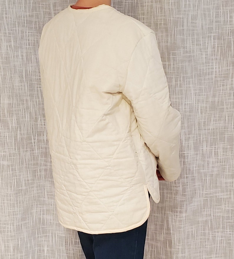 May include: A white quilted jacket with a long sleeve and a diamond pattern. The jacket has a stand-up collar and a zipper closure.