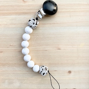 Peut inclure: Un hochet pour bébé en silicone blanc et noir avec un clip en bois noir et une ficelle noire.
