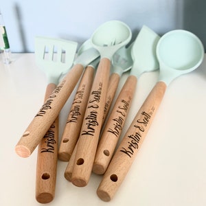 May include: A set of six wooden handled kitchen utensils with light blue silicone heads. The handles are engraved with the names "Kristin & Scott" and the date "October 22, 2022".