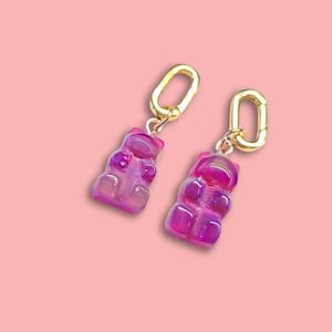 May include: A pair of gold dangle earrings with purple gummy bear charms.