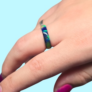 May include: A ring with a blue, green, and yellow swirl pattern. The ring is on a person's finger.