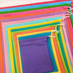 May include: A set of 17 colourful drawstring bags made of fabric. The bags are arranged in a rainbow pattern, with the smallest bag in the centre and the largest bag on the outside.