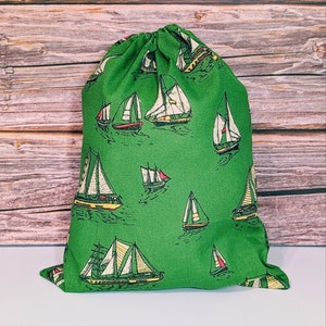 Peut inclure: Sac à cordon vert avec un motif de voiliers blancs et jaunes. Le sac est en tissu et possède une fermeture à cordon.