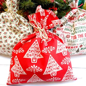 May include: Three festive Christmas gift bags. One is red with white Christmas trees, another has a holly pattern, and the third has holiday phrases. Each bag is tied with twine.
