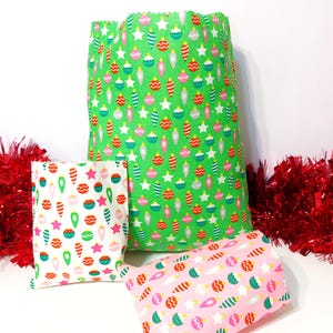 May include: Three Christmas gift bags in different sizes. The largest bag is green with a pattern of baubles and stars. The smaller bags have similar bauble patterns on white and pink backgrounds. Red tinsel is in the background.