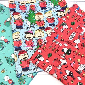 May include: Three fabric swatches with Christmas-themed patterns. One is teal with Snoopy, Christmas trees, and Charlie Brown. Another is light blue with the Peanuts gang singing carols. The third is red with Snoopy and holiday elements.