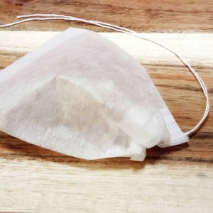 May include: A white tea bag with a drawstring, sitting on a wooden surface.