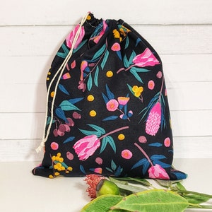 May include: A black reusable shopping bag with a floral print featuring pink, yellow, and green flowers on a black background. The bag has a drawstring closure and is made of cotton.