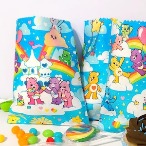 May include: Three blue and white gift bags with a rainbow and Care Bear design. The bags feature a variety of Care Bears, including Cheer Bear, Funshine Bear, and Good Luck Bear. The bags are perfect for a birthday party or any special occasion.