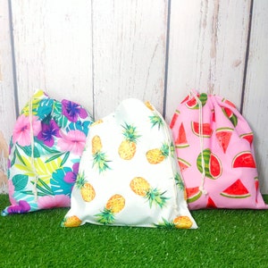 May include: Three drawstring bags with different tropical fruit prints. One bag has a pink background with watermelon slices, another has a white background with pineapple slices, and the last has a pink background with tropical flowers and leaves.