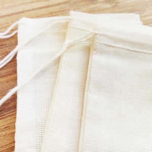 May include: Three white cotton muslin bags with drawstring closures. The bags are folded and stacked on top of each other.