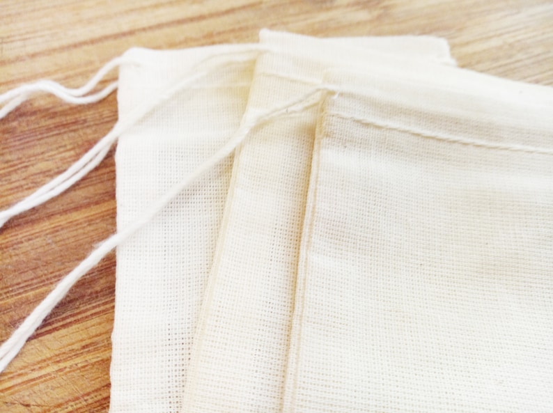 May include: Three white cotton muslin bags with drawstring closures. The bags are folded and stacked on top of each other.