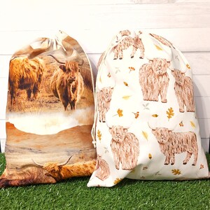 Brown Highland cow gift bags, reusable fabric drawstring bags. One bag has a hyperrealistic fabric of Highland Cows and scenery. The second bag features sketched cows with Autumn leaves on a white background