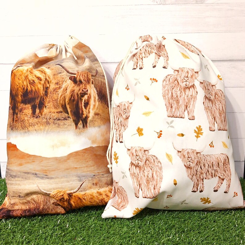 Brown Highland cow gift bags, reusable fabric drawstring bags. One bag has a hyperrealistic fabric of Highland Cows and scenery. The second bag features sketched cows with Autumn leaves on a white background