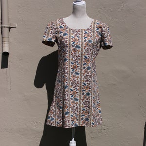 May include: A white dress with a floral print and short sleeves. The dress is on a white mannequin and has a brown, orange, and blue floral pattern.