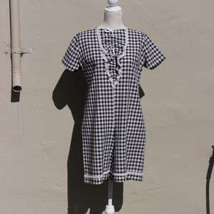 May include: A black and white gingham print dress with short sleeves and a white lace trim. The dress is displayed on a white mannequin. The dress has a ruffled detail down the front.