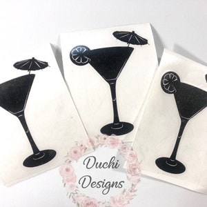 May include: Three white art prints featuring a black martini glass design. Each print shows a martini glass with a lemon slice and a small parasol. The prints are displayed on a white surface.