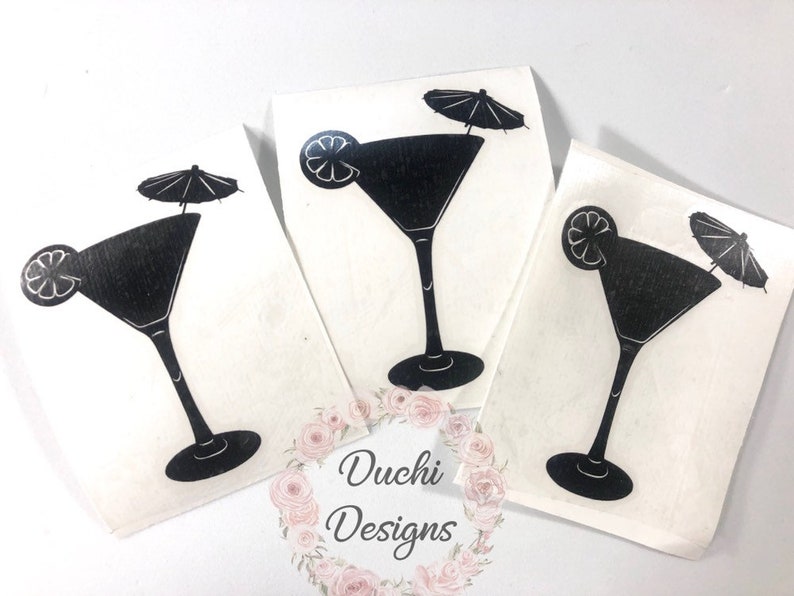 May include: Three white art prints featuring a black martini glass design. Each print shows a martini glass with a lemon slice and a small parasol. The prints are displayed on a white surface.