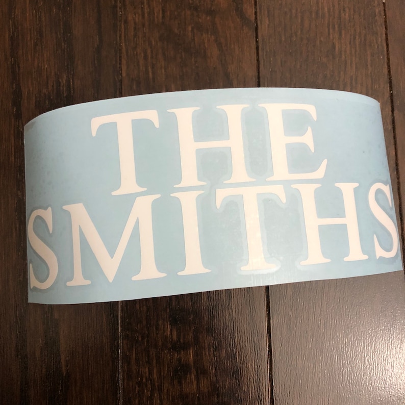 May include: A light blue vinyl decal featuring the white text "THE SMITHS" in uppercase. The decal is curved, suggesting it's ready for application. The lettering is in a clear, traditional font, suitable for various surfaces.