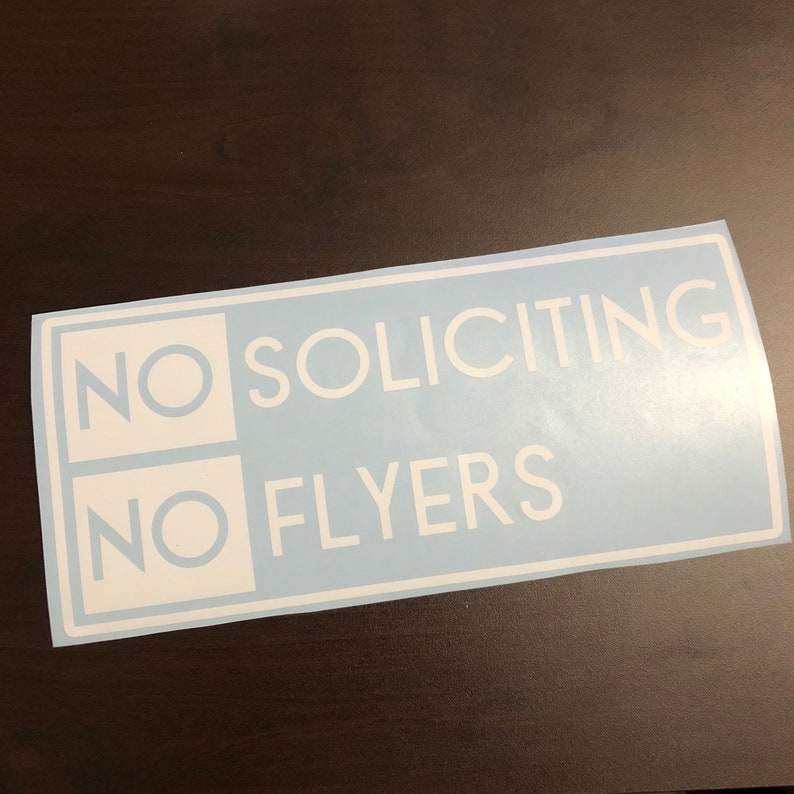 May include: A blue and white sticker with the text "NO SOLICITING NO FLYERS" in white lettering.